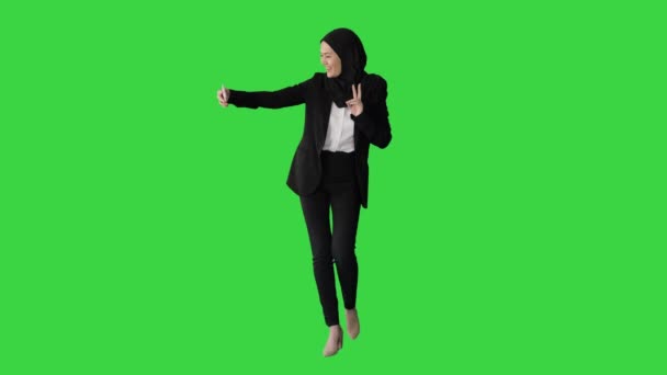 Mosolygó arab nő hidzsábban szelfiket készít a mobilján, miközben egy zöld vásznon sétál, Chroma Key. — Stock videók
