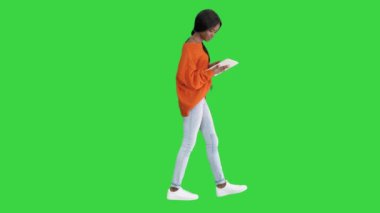 Gülümseyen Afrikalı Amerikalı kadın yeşil ekranda yürürken tablet kullanıyor, Chroma Key.
