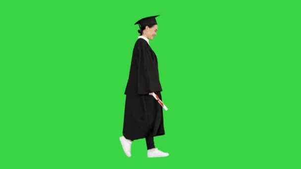 Leende kvinna student i examen mantel promenader med sitt diplom på en grön skärm, Chroma Key. — Stockvideo