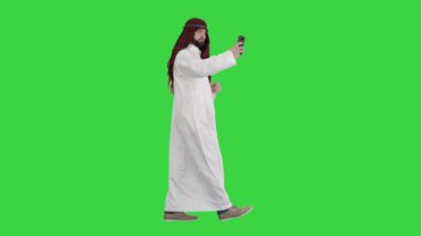 Yeşil Ekran, Chroma Key 'de yürüyen ve telefonuyla selfie çeken Arap bir adam..