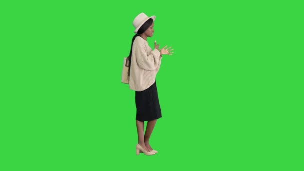 Ung afrikansk amerikansk kvinna i stickade kläder och vit hatt pratar och gester på en grön skärm, Chroma Key. — Stockvideo