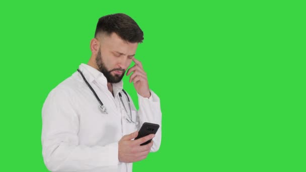 Beyaz üniformalı bir erkek doktor yeşil ekranda yürür ve akıllı telefon kullanır, Chroma Key. — Stok video