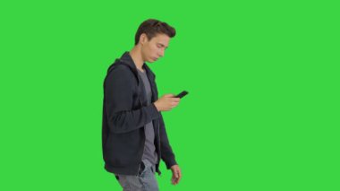 Yeşil Ekran 'da yürürken, Chroma Key' de yürürken ve cep telefonuyla mesajlaşırken günlük kıyafetlerle dolaşan genç adam..