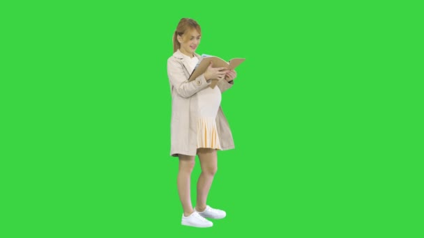 La mujer embarazada de pie con un libro sobre una pantalla verde, Chroma Key. — Vídeos de Stock