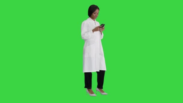 Χαμογελώντας αφροαμερικανίδα γιατρός γραπτών μηνυμάτων σε smartphone σε μια πράσινη οθόνη, Chroma Key. — Αρχείο Βίντεο