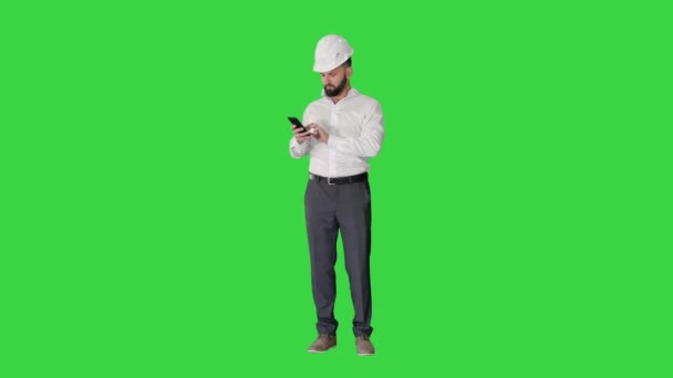 聪明的工程师，身穿白衬衫，头戴安全工程帽，在绿色屏幕上使用智能手机，铬钥匙. — 图库视频影像