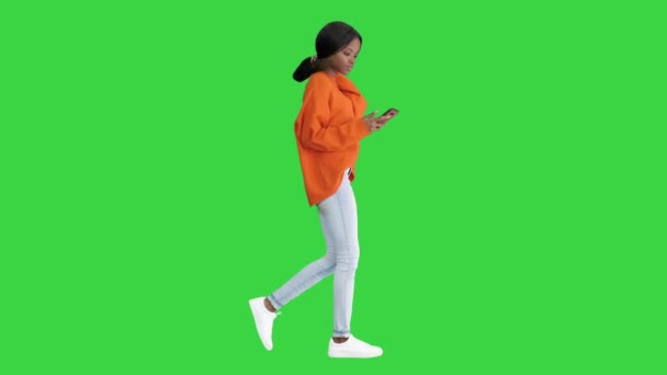 緑の画面、クロマキーを歩いている間、彼女の携帯電話にテキストメッセージを入力する笑顔の女性. — ストック動画