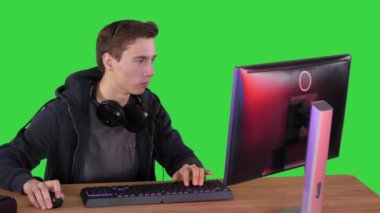 Kulaklıklı oyuncu bilgisayarda video oyunu oynuyor ve Yeşil Ekran, Chroma Key 'de başparmağını kameraya gösteriyor..