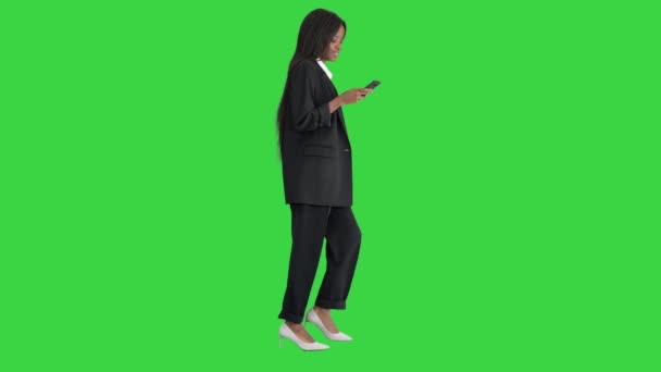 緑の画面、クロマキーを歩いている間に携帯電話でアフリカ系アメリカ人女性のテキストを微笑む. — ストック動画