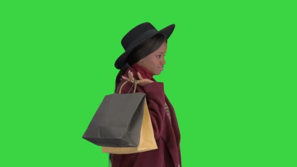 Όμορφο κορίτσι της αφρικανικής μόδας με παλτό και μαύρο καπέλο βόλτα με τσάντες ψώνια σε μια πράσινη οθόνη, Chroma Key. — Αρχείο Βίντεο