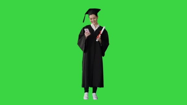 Boldog női diplomás kezében diploma és sms-ezés a telefonján egy zöld képernyőn, Chroma Key. — Stock videók