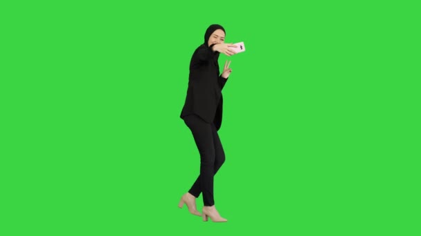 Femme arabe souriante dans le hijab prendre selfies sur son téléphone portable comme elle marche sur un écran vert, Chroma Key.