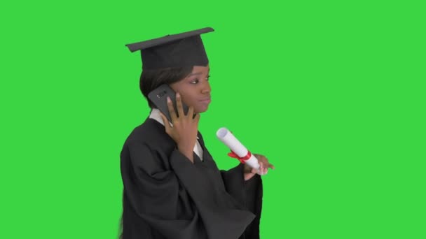 Estudiante afroamericana en bata de graduación hablando por teléfono mientras camina en una pantalla verde, Chroma Key. — Vídeo de stock