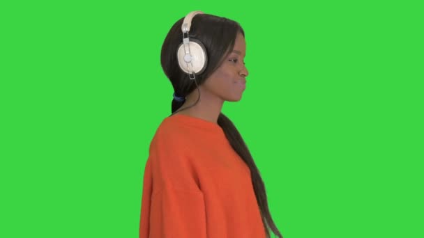 Donna afroamericana sorridente con cuffie che cammina ascoltando la musica su uno schermo verde, Chroma Key. — Video Stock