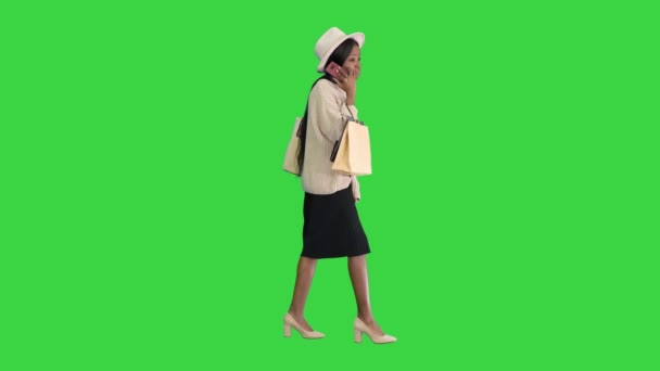 Afroamerikansk tjej i överdimensionerade stickade kläder och mössa pratar på sin telefon medan hon går med shoppingväskor på en grön skärm, Chroma Key. — Stockvideo