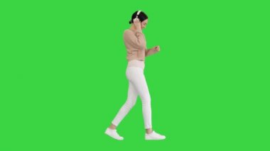 Yeşil ekranda yürüyen ve dans eden kulaklıklı gülümseyen kadın, Chroma Key.