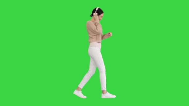 Uśmiechnięta kobieta ze słuchawkami chodzącymi i tańczącymi do muzyki na zielonym ekranie, Chroma Key. — Wideo stockowe