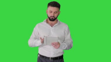 Ciddi genç yönetici dijital tablet kullanıyor ve yeşil ekran, kroma anahtar üzerinde anlaşan kameraya bakıyor.