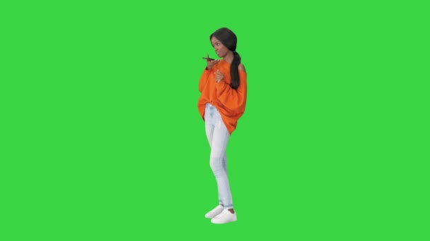 Ładna Afroamerykanka w jasnym swetrze dyktuje wiadomość za pomocą telefonu na zielonym ekranie, Chroma Key. — Wideo stockowe