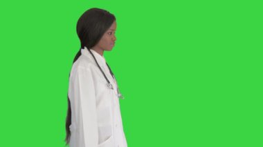 Üzgün Afrikalı Amerikalı kadın doktor elini cebine atarak yeşil ekranda yürüyor, Chroma Key.