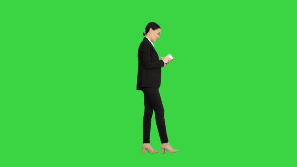 Concentrated woman in a suit writing business ideas in her notepad while walking on a Green Screen, Chroma Key. — Stock Video