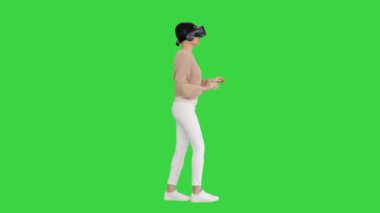 Yeşil Ekran, Chroma Key 'de yürüyen ve etkileşimli VR kulaklık kullanan sevimli genç bir kadın..