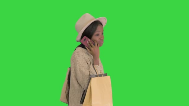 Ragazza afroamericana in maglieria oversize e cappello parlando sul suo telefono mentre cammina con le borse della spesa su uno schermo verde, Chroma Key. — Video Stock