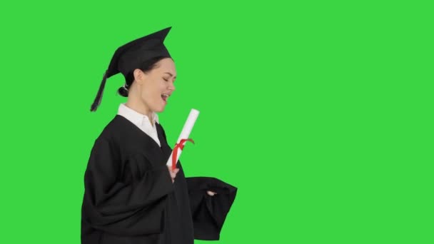 Feliz estudiante femenina en bata de graduación caminando y animando con su diploma en una pantalla verde, Chroma Key. — Vídeos de Stock