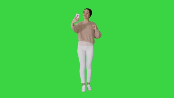 Sorridente giovane donna che ha videochiamata sul suo telefono agitando mano su uno schermo verde, Chroma Key. — Video Stock