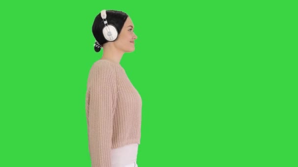 Jovem com fones de ouvido andando ouvindo a música em uma tela verde, Chroma Key . — Vídeo de Stock