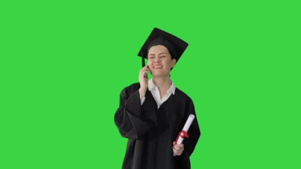 졸업 예복을 입은 행복 한 여학생이 그린 스크린 (Green Screen) 크로마 키 (Chroma Key) 에서 졸업장을 받고 걸어 다닐 때 감정적으로 전화로 이야기하는 모습.. — 비디오
