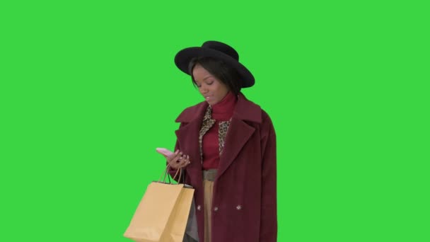 Улыбающаяся африканская модница в пальто и черной шляпе, текстурирующая на телефоне на зеленом экране, Chroma Key. — стоковое видео