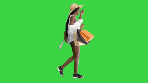 Glad afrikansk amerikansk kvinna i halmhatt promenader med shoppingväskor på en grön skärm, Chroma Key. — Stockvideo