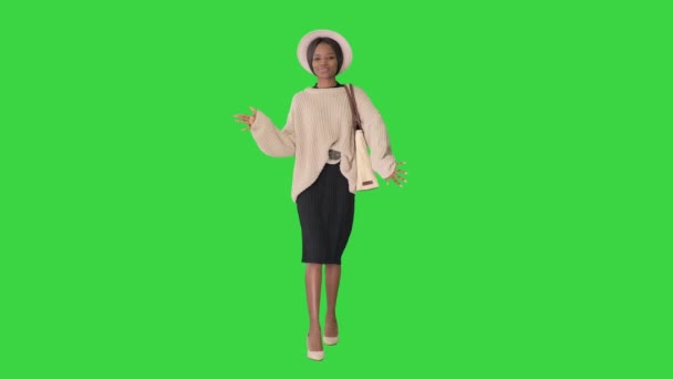 Stijlvolle Afrikaans-Amerikaanse vrouw in gebreide kleding en witte hoed dansen tijdens het lopen op een groen scherm, Chroma Key. — Stockvideo