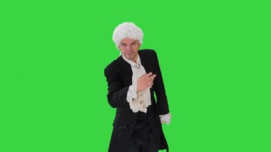 Eski moda dantelli cüppeli ve beyaz peruklu bir adam yeşil ekran Chroma Key 'de kameraya bakarak fiyonk yapıyor..