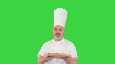 Elinde pizzayla çekici bir aşçı Yeşil Ekran 'da yürüyor ve kamerayla konuşuyor, Chroma Key..