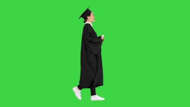 Feliz estudiante femenina en bata de graduación caminando y animando con su diploma en una pantalla verde, Chroma Key. — Vídeo de stock