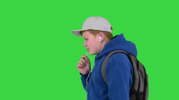 Tiener jongen bellen op mobiele telefoon met behulp van handsfree tijdens het lopen op een groen scherm, Chroma Key. — Stockvideo