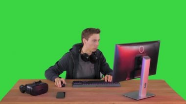 Kulaklıklı oyuncu bilgisayarda video oyunu oynuyor ve Yeşil Ekran, Chroma Key 'de başparmağını kameraya gösteriyor..