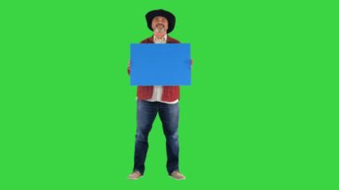 Yeşil ekranda boş bir levha tutan şapkalı kıdemli çiftçi, Chroma Key..