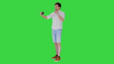 Günlük beyaz gömlekli genç adam yeşil ekranda, Chroma Key 'de telefonuyla selfie çekiyor..