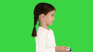 Gülümseyen küçük kız elinde kumandayla oyun oynuyor. Elinde yeşil ekran, Chroma Key var..