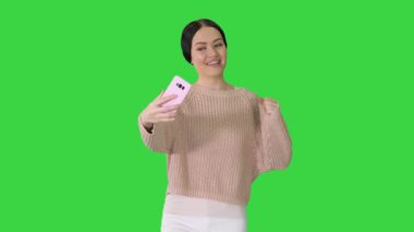 Duygusal, genç bir bayan, yeşil ekranda yürürken telefonuyla video konuşmasını bitiriyor, Chroma Key..