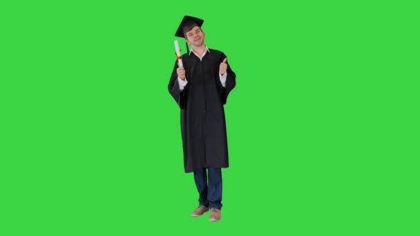 Glückliche männliche Student in Abschlussrobe posiert mit seinem Diplom und zeigt Daumen nach oben auf einem Green Screen, Chroma Key. — Stockvideo