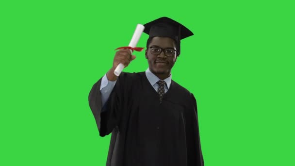 Happy Afro-Amerikaanse mannelijke student in afstuderen badjas lopen in de richting van camera zwaaien zijn diploma op een groen scherm, Chroma Key. — Stockvideo