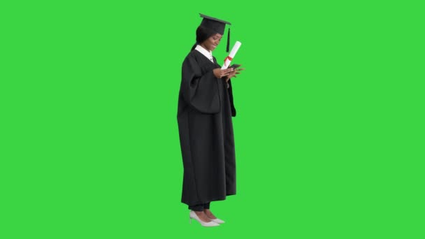 Boldog afro-amerikai női diplomás kezében diploma és SMS-t a telefonján egy zöld képernyőn, Chroma Key. — Stock videók