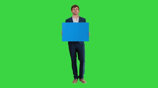 Joven hombre de negocios sosteniendo un cartel en blanco mirando a la cámara en una pantalla verde, Chroma Key. — Vídeo de stock
