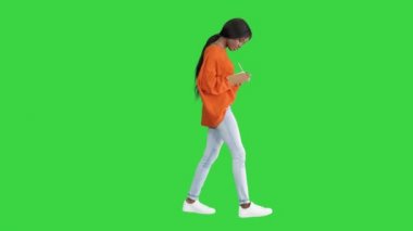 Yeşil ekranda yürürken, parlak kazaklı güzel Afrikalı Amerikalı kadın not defterine Chroma Key yazıyor..