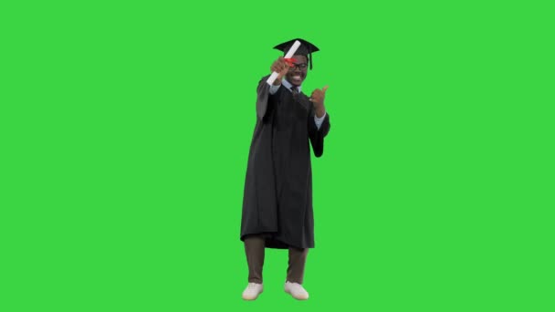 Eccitato studente afroamericano maschio in vestaglia di laurea rinunciare al suo diploma e in posa per la fotocamera su uno schermo verde, Chroma Key. — Video Stock