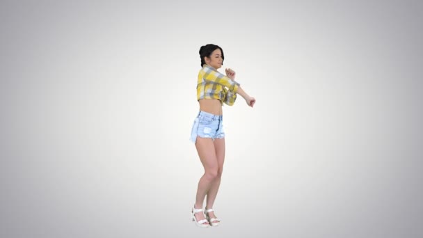 Ragazza in camicia quadrata e pantaloncini jeans, scarpe da ginnastica, danza su sfondo sfumato. — Video Stock